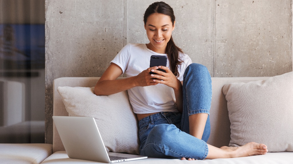 Happy woman is using phone and laptop
