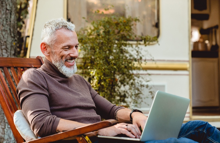 Senior male traveler working on his laptop in deck chair in the RV park